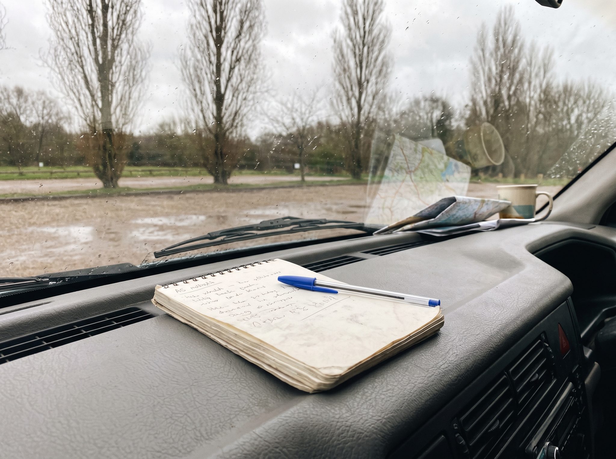 Carnet et stylo posés sur le tableau de bord d'un camping-car, matin gris